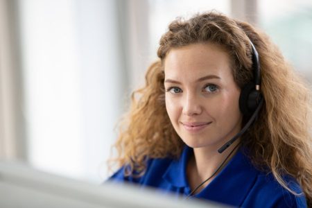 Hotline Support Service. call center operator in headset working with laptop in modern office, looking at computer screen, free space